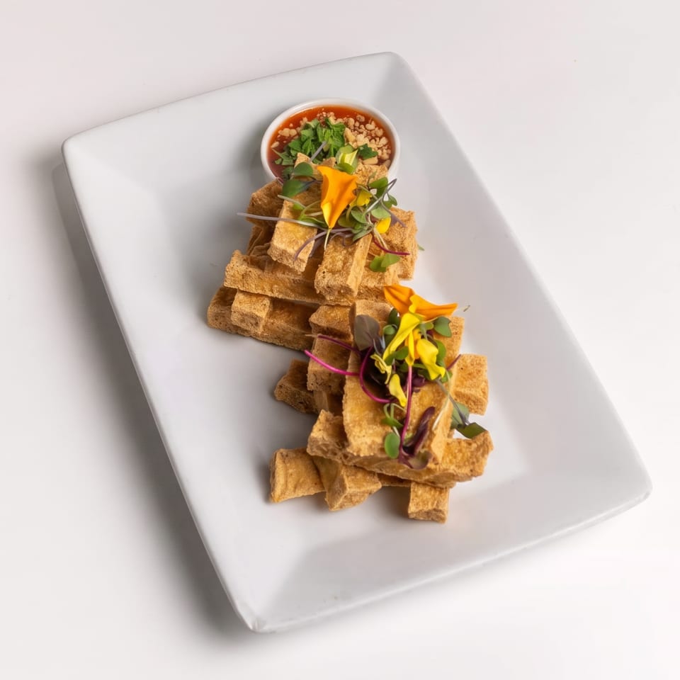 Two stacks of crispy fried tofu with microgreens, edible flowers, and a peanut dipping sauce.